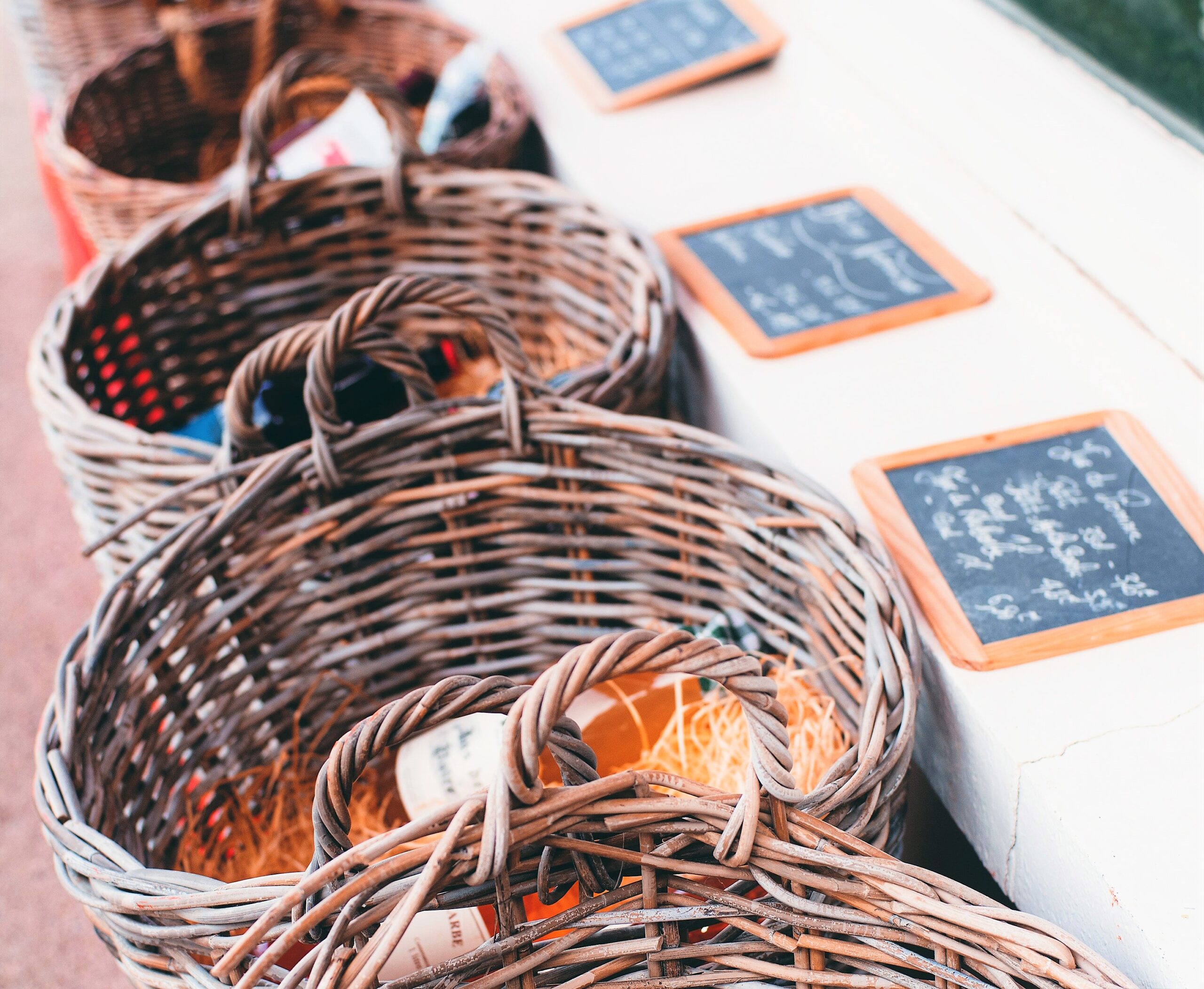 Wicker baskets are presented in front of a long white counter displaying old fashioned individual chalk boards with inscriptions on it.