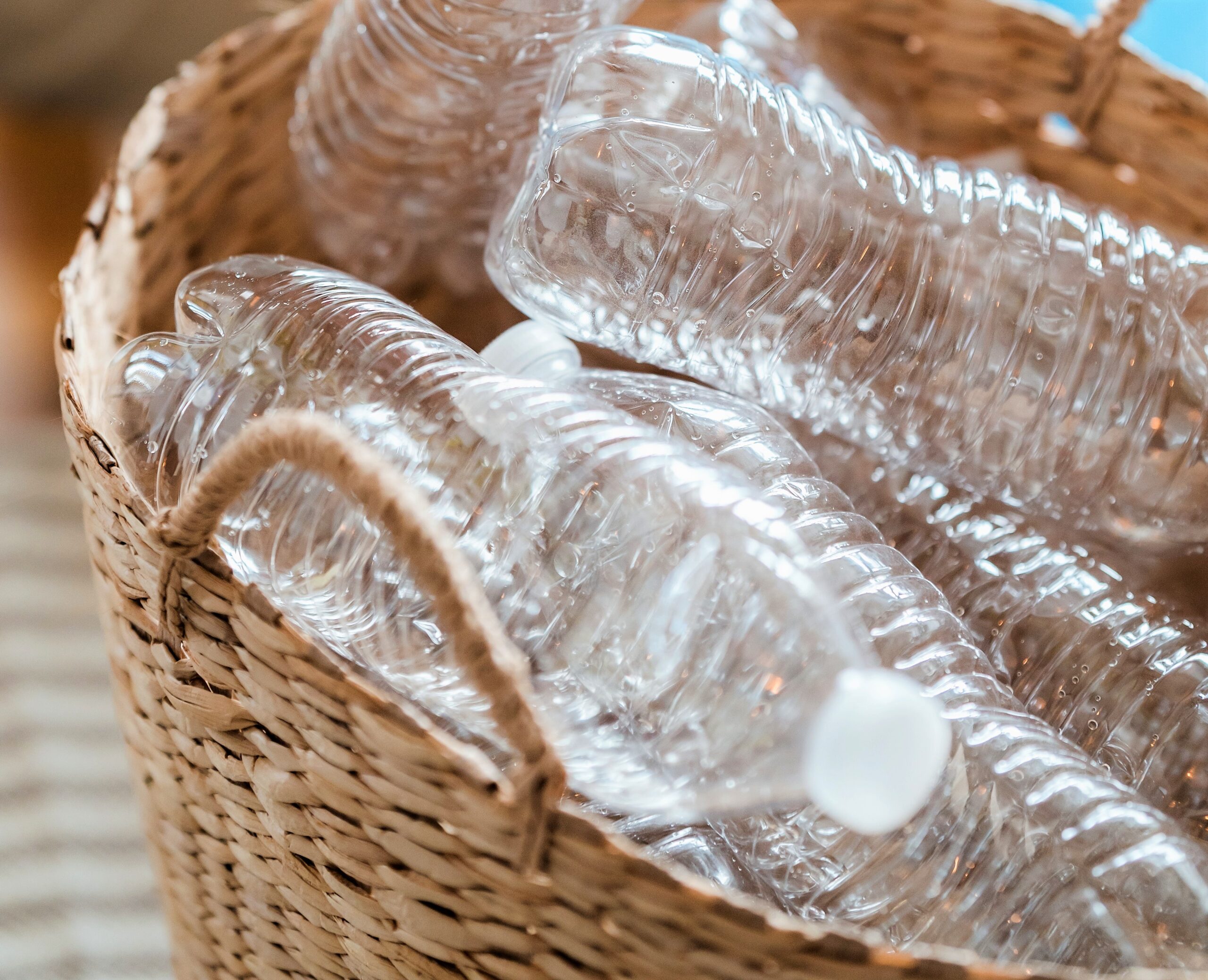 A nice wicker basket is overfilled with empty plastic water bottles.