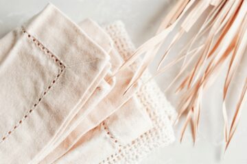 Natural white napkins with detailed borders are resting on a crisp bright white linen tablecloth.