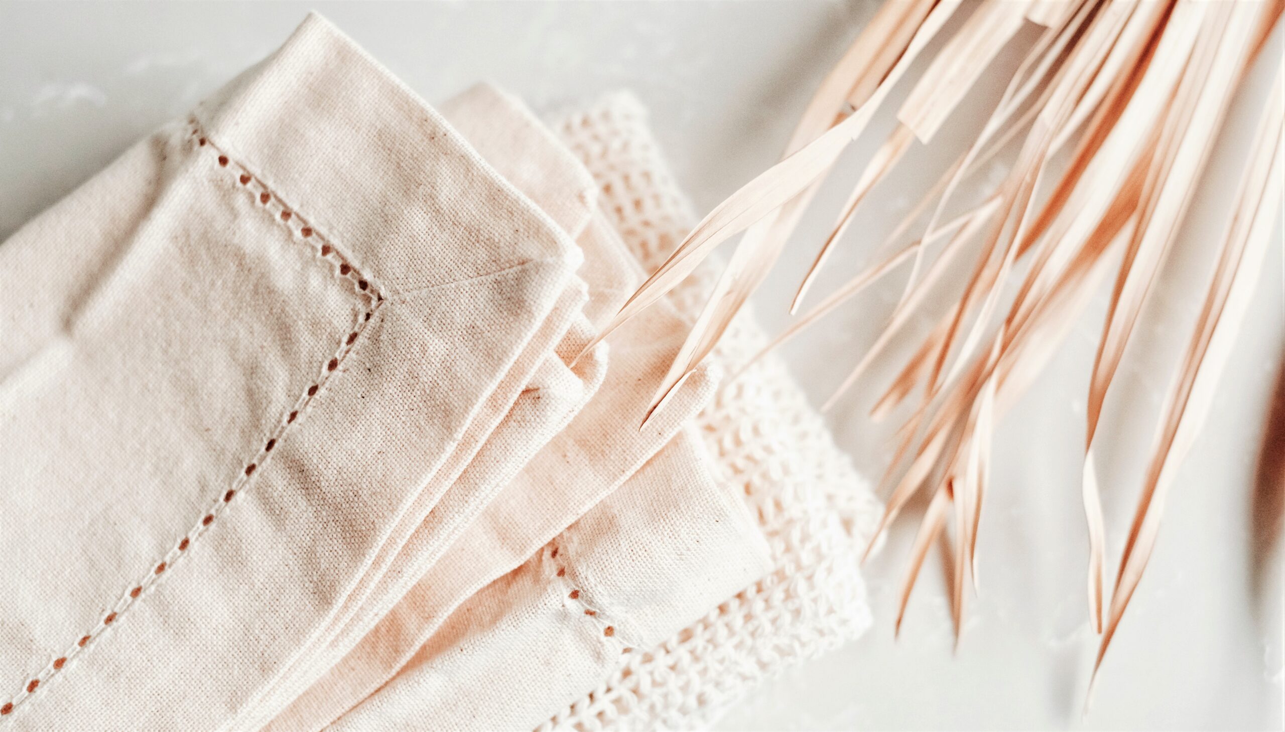 Natural white napkins with detailed borders are resting on a crisp bright white linen tablecloth.