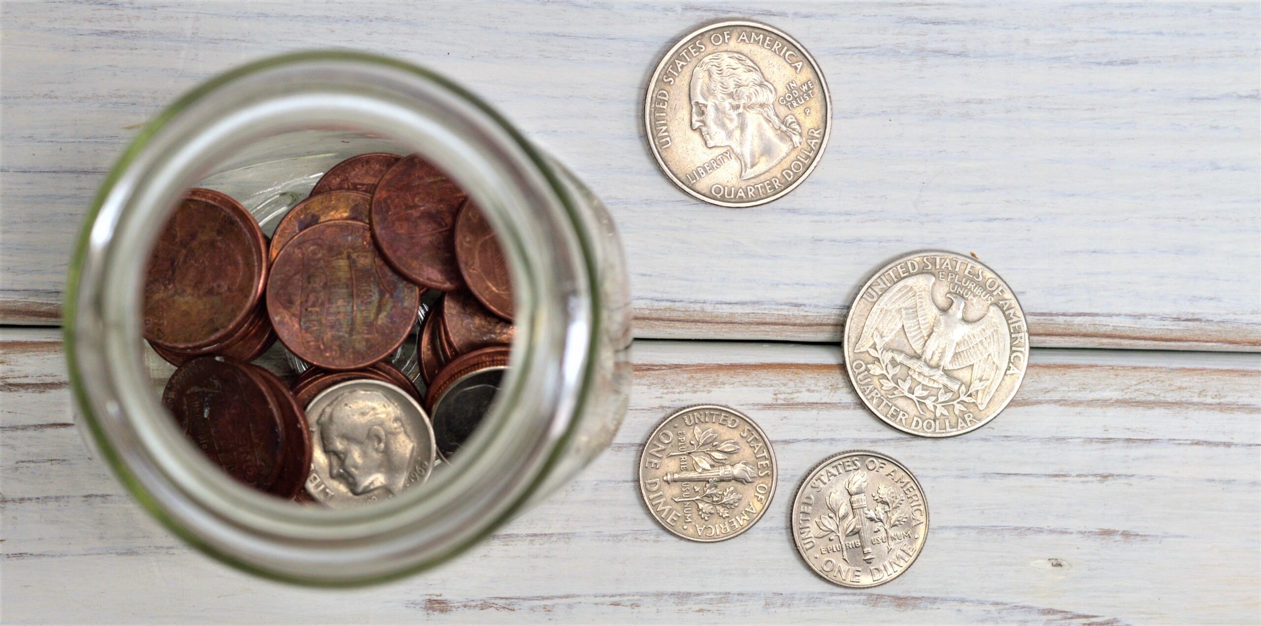 A jar filled with coins is sitting on a whitewashed board table.