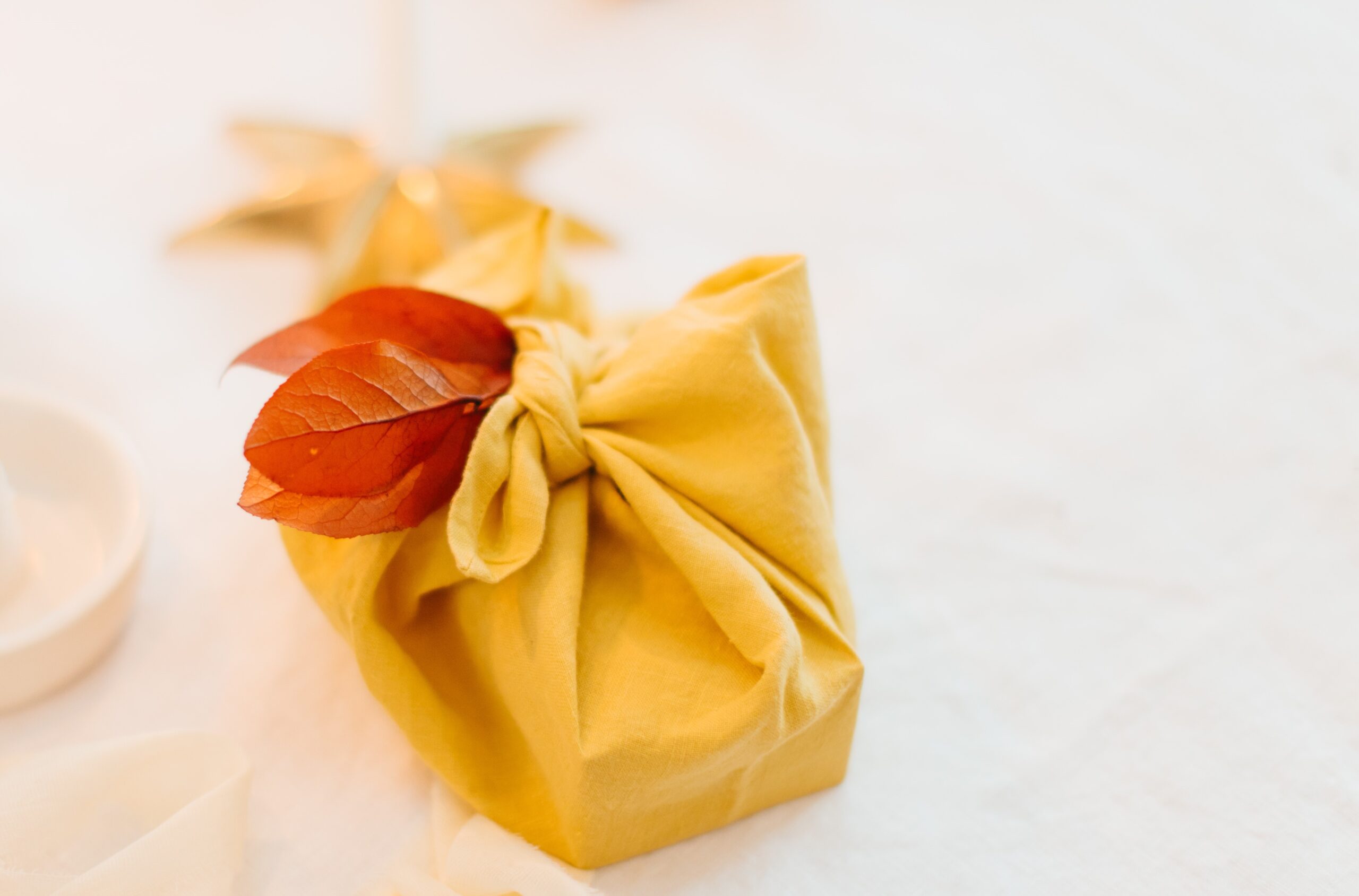 A present brightly wrapped in a yellow furoshiki is set on a table adorned with a white tablecloth.