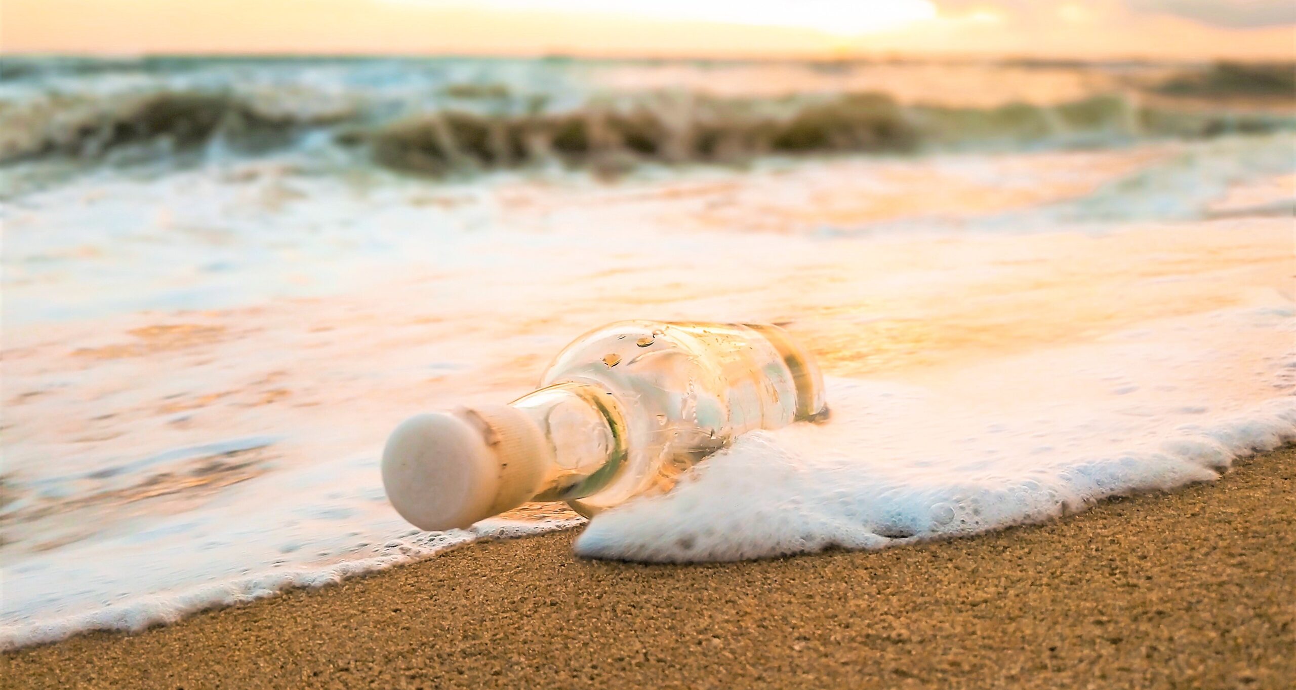 A bottle with a message inside has been washed ashore, laying on the sandy beach.
