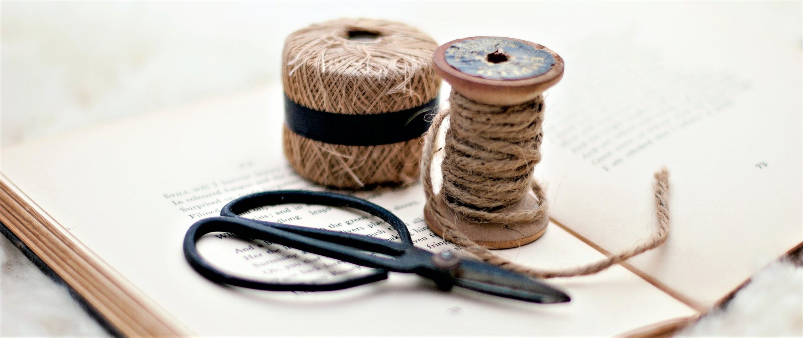 Two spools of twine are resting on an open book with a pair of metal scissors by their side.