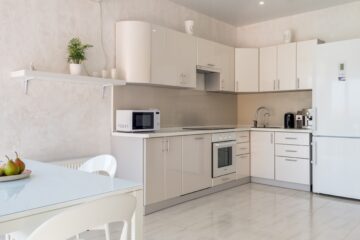 A white open concept kitchen features sleek porcelain floors and a perfect cooking triangle.